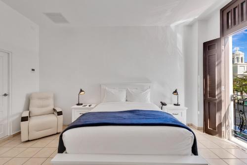 a white bedroom with a large bed and a chair at Armas Hotel in San Juan