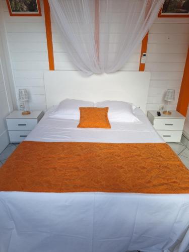 a bedroom with a large white bed with an orange pillow at Bungalow les Cerisiers in Bouillante