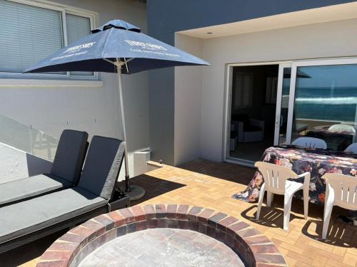 a patio with a table and an umbrella and chairs at Jongensfontein Beachside Villa in Jongensfontein
