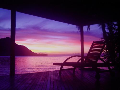 a chair sitting on a porch watching the sunset at Robinson's Cove Villas - Deluxe Cook Villa in Papetoai