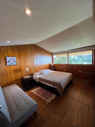 a bedroom with a bed and a couch and a window at Cabaña Guarumo de la Sierra - Minca in El Campano