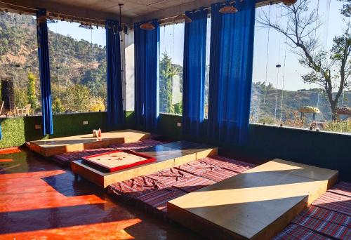a room with tables and large windows with blue curtains at Hill Ventures Adventure Camp and Restaurant in Dharamshala