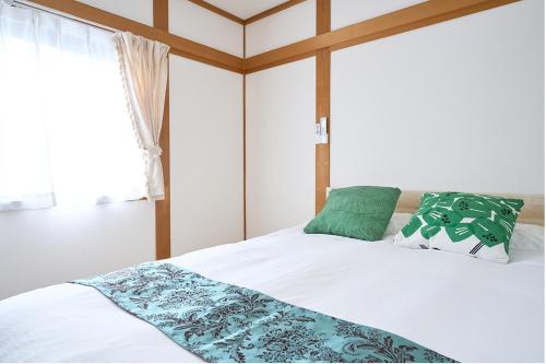 a bedroom with a bed with white sheets and green pillows at KANAKO GUEST HOUSE 1号館 osaka in Osaka