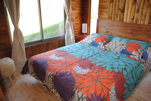 a bed with a colorful comforter in a room with a window at Cabañas & SPA Carilafquen in Laguna Verde