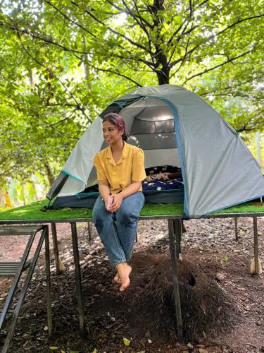 a woman sitting on a table in front of a tent at Dragster Tents in Kizhake Chālakudi