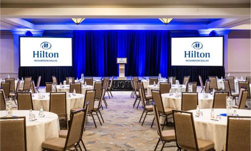 a conference room with tables and chairs and two screens at Hilton Richardson Dallas, TX in Richardson