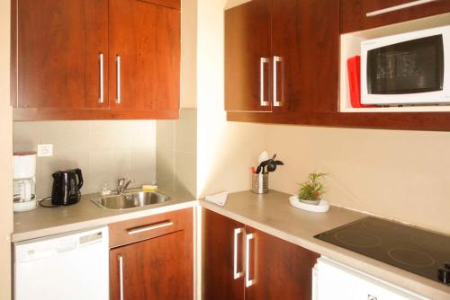 a small kitchen with wooden cabinets and a microwave at Comfort Aparthotel Marseille Prado in Marseille