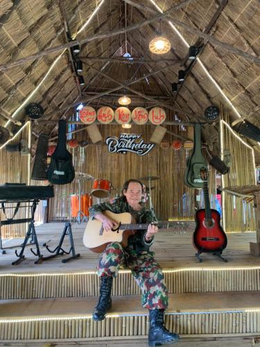 a man sitting on a stage playing a guitar at Khu Du Lịch Sinh Thái, Nghỉ dưỡng Homestay Hoàng Ánh - Kon Xom Luh in Kon Tum