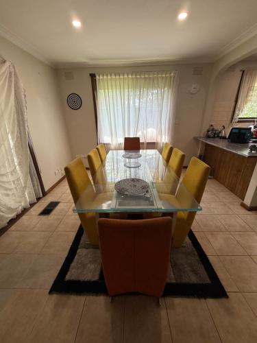a dining room with a glass table and yellow chairs at Bundoora cozy room in Melbourne