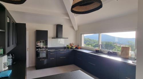 une cuisine avec des armoires noires et une grande fenêtre dans l'établissement Maison de standing avec piscine vue mer Corse du sud de 6 à 14 personnes 7 chambres, à Coti-Chiavari