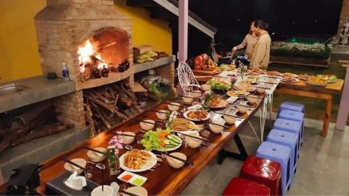 a long table with plates of food and a fireplace at Hồ Bơi Vô Cực - Có Thể Săn Mây Tại Giường in Da Thanh