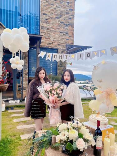 two women holding a bouquet of flowers at a party at Hồ Bơi Vô Cực - Có Thể Săn Mây Tại Giường in Da Thanh