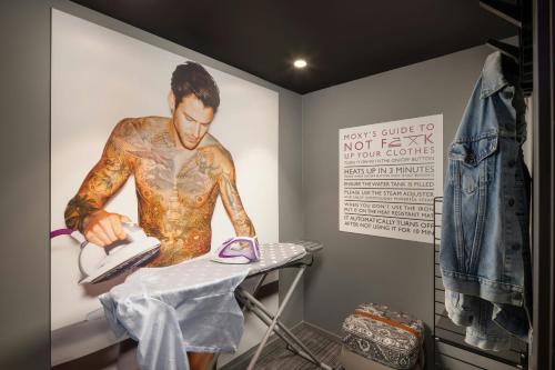 a man with tattoos cutting a shirt in a room at Moxy Glasgow Merchant City in Glasgow