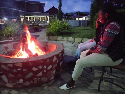 two women sitting in chairs next to a fire pit at Olempiaus Gardens Hotel in Mai Mahoro