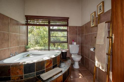 bagno con vasca, servizi igienici e finestra di Woodlandsbushlodge a Hoedspruit