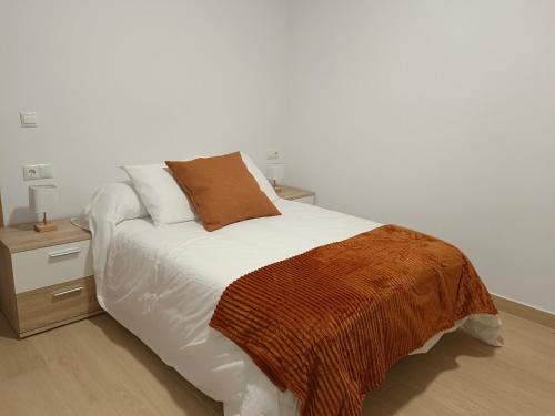 a white bed with a brown blanket and a night stand at Apartamentos La Fuente in Almodóvar del Río