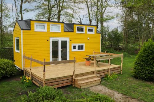 a yellow tiny house with a deck in a yard at Tinyhouse Horssen in Bergharen