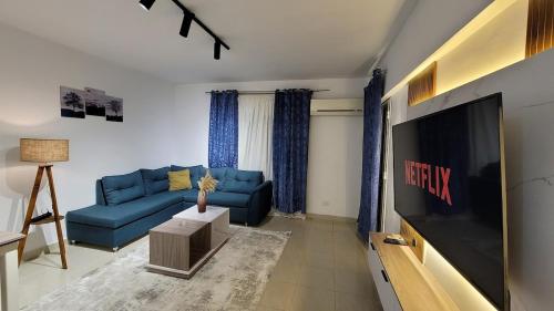 un salon avec un canapé bleu et une télévision à écran plat dans l'établissement Rehab Elegant Apartment - New Cairo, à Burg el-Ḥudûd