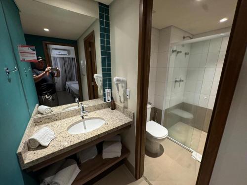 a man taking a picture of a bathroom with a sink and shower at Apto Solar das Águas Olimpia SP in Olímpia