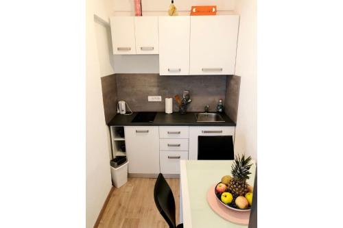 a kitchen with white cabinets and a bowl of fruit on a table at Apartment Bonaca in Rogoznica