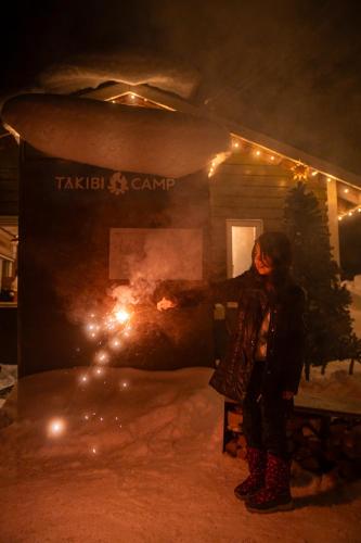 a woman standing in the snow in front of a building at 焚き火キャンプ場 Hokkaido Glamping - TAKIBI in Makkari