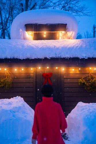 a man walking past a garage with snow and lights at 焚き火キャンプ場 Hokkaido Glamping - TAKIBI in Makkari