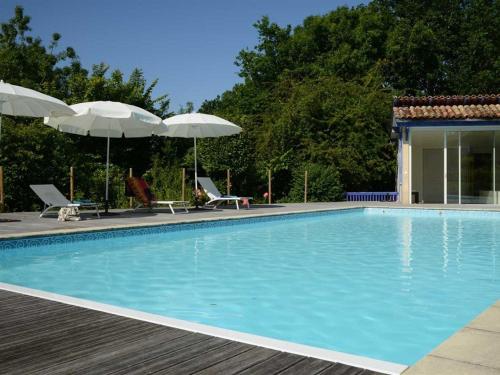 a swimming pool with two umbrellas and chairs at Chambres d'Hôtes La Sauvageonne in Saint-Palais