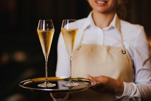 a woman holding two glasses of champagne on a tray at Stock Exchange Hotel, Manchester, Autograph Collection in Manchester