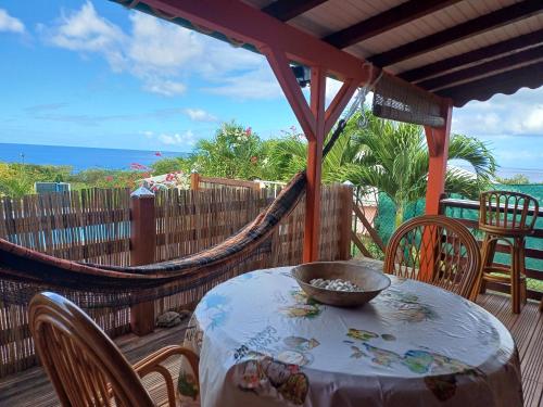 a table and chairs on a porch with a hammock at Soleil couchant in Bouillante