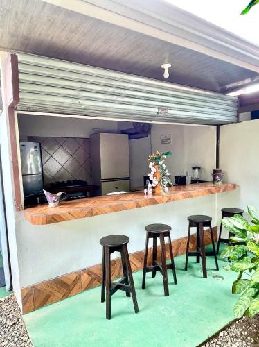 a bar with four stools in front of a kitchen at Villas Ela en Bahía Ballena,Uvita Hermosas habitaciones privadas grandes, piscina, cocina, jacuzzi, aire acondicionado, tv y baño privado in Uvita