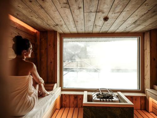 a woman sitting in a sauna looking out the window at SPA & Naturhotel Outside in Matrei in Osttirol
