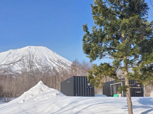 a snow covered mountain with a building and a tree at 焚き火キャンプ場 Hokkaido Glamping - TAKIBI in Makkari