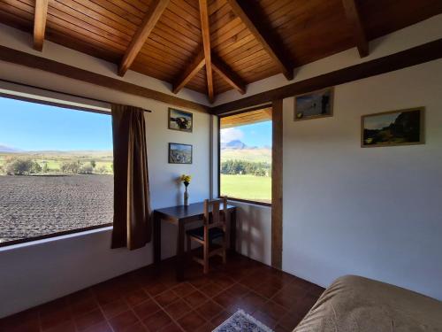 a bedroom with a bed and a desk and windows at Cotopaxi Lodge in Hacienda Porvenir