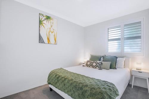 a white bedroom with a bed with a green blanket at Greenslopes Cityview Haven in Brisbane