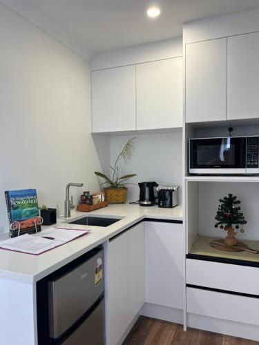 a white kitchen with a sink and a microwave at Cozy sleepout in Hamilton