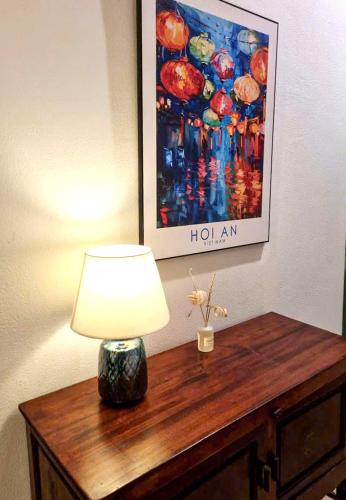 a lamp on a wooden table with a painting on the wall at House Happy Clam Hoi An in An Bang