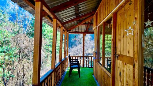 a porch of a cabin with two chairs on it at Rustic Mud House Jibhi in Jibhi