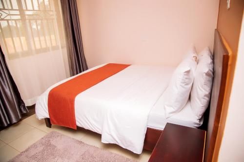 a bedroom with a bed with white sheets and an orange blanket at Blue Berries Hotel in Entebbe