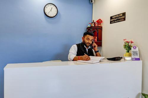 a man sitting at a desk talking on a cell phone at Hotel Warm Welcome Inn - Noida Sector 26 in Noida