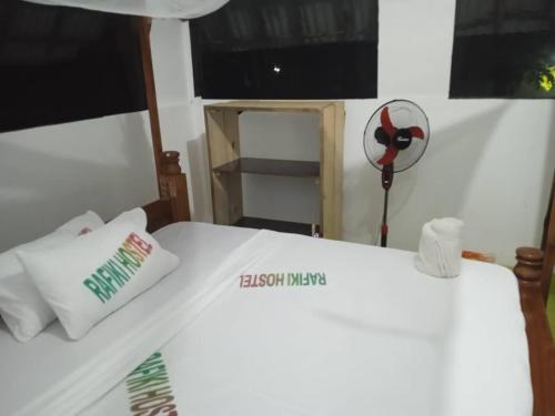 a white bed with two pillows and a fan at Rafiki Backpackers-hostel in Nungwi