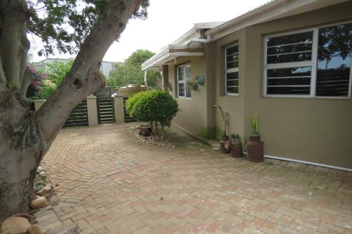 a house with a brick driveway next to a tree at Destiny Jeffreys bay in Jeffreys Bay