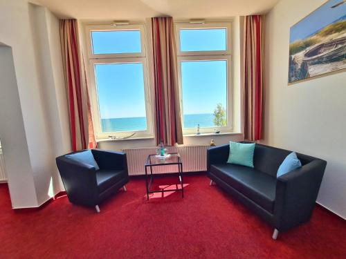 a living room with two chairs and a table and two windows at Zeitlos Hotel Garni in Scharbeutz