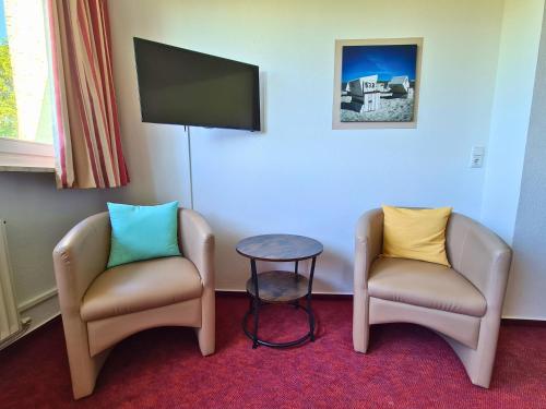 two chairs and a table in a room with a tv at Zeitlos Hotel Garni in Scharbeutz