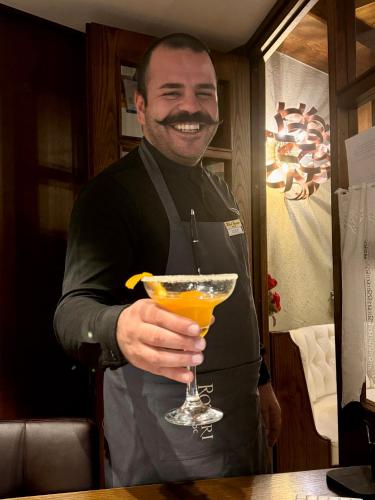 a man in an apron holding a drink at Hotel Europa in San Martino di Castrozza