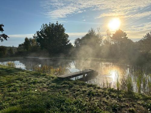 a misty lake with a dock in front of the sun at Agroturystyka Złoty Klon Drewniany Domek in Kijanka