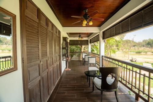 a porch with a ceiling fan and tables and chairs at Akara House Sukhothai - Luxury Riverside Residence in Sukhothai