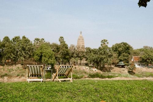 two chairs sitting in the grass in a field at Akara House Sukhothai - Luxury Riverside Residence in Sukhothai