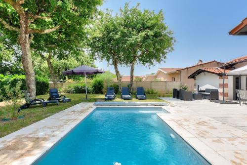 - une piscine dans une cour avec des chaises et un parasol dans l'établissement Maison de la Source - Piscine chauffée, proche plage du Betey, à Andernos-les-Bains