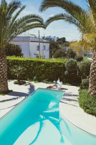a woman sitting next to a swimming pool with palm trees at Savito Guest House in Martina Franca