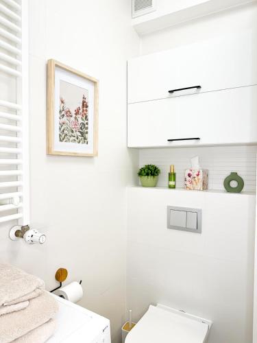 a white bathroom with a toilet and a picture on the wall at Apartamenty Prestige Harmony Rosiczkowa in Augustów